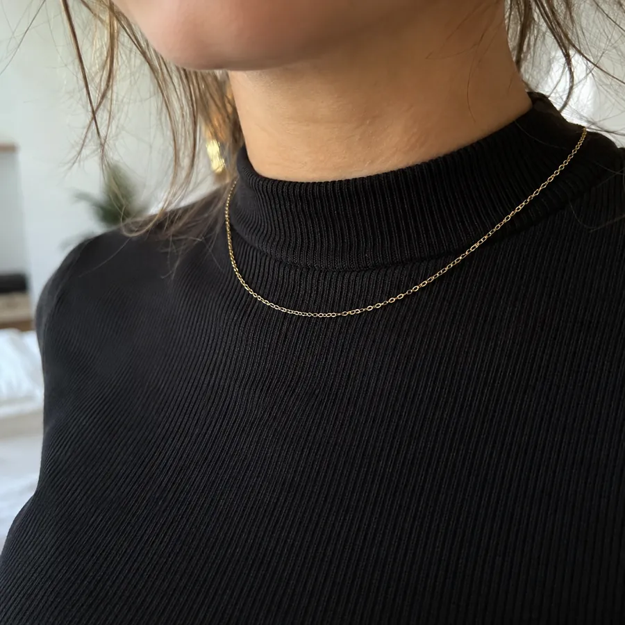Close-up of a black fitted top with a high band collar and a thin gold chain