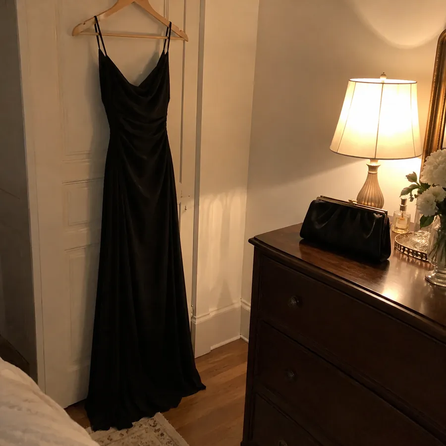 Long black crepe evening gown on a hanger beside a black satin clutch